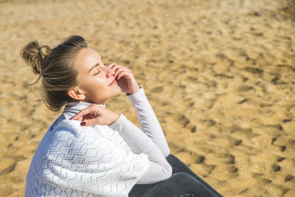 Woman sitting on sand sunbathing in sofa sunlight. Mindfulness and slow living concept.