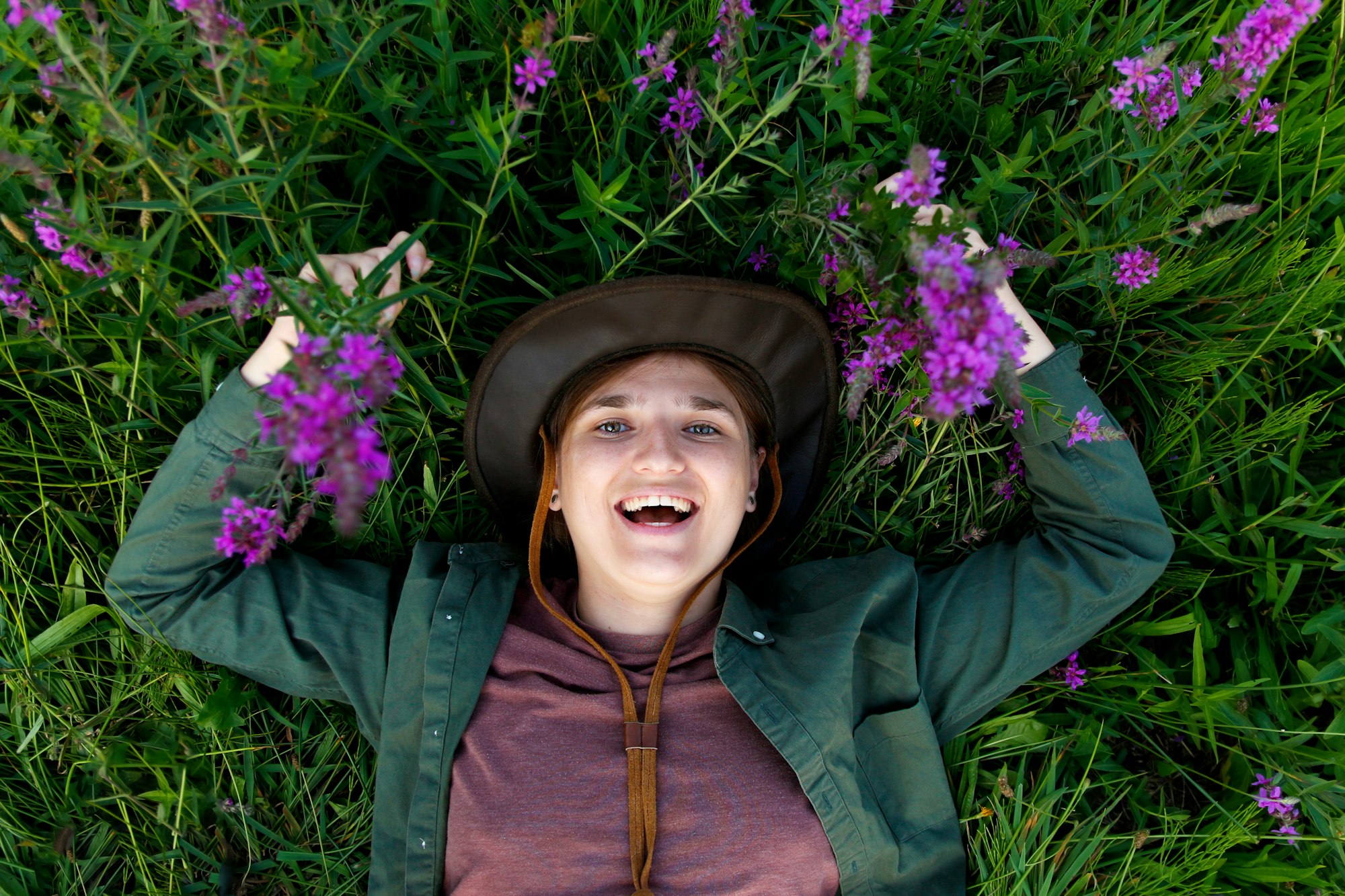 Funny woman lying in summer grass and purple flowers. Wellness. Hello summer. Top view. Summertime.