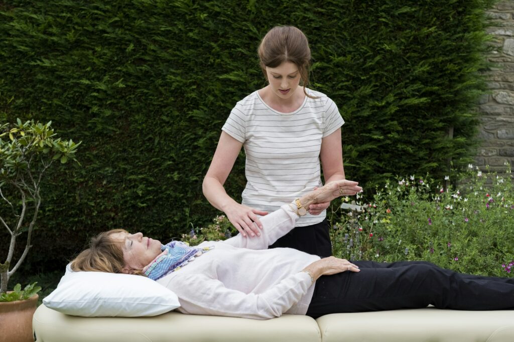 Reiki therapist with a client in a therapy session touching meridian points on the body.
