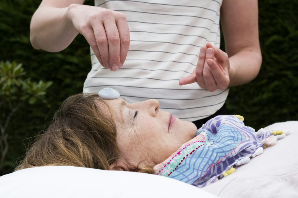 Reiki therapist with a client in a therapy session touching meridian points on the body.